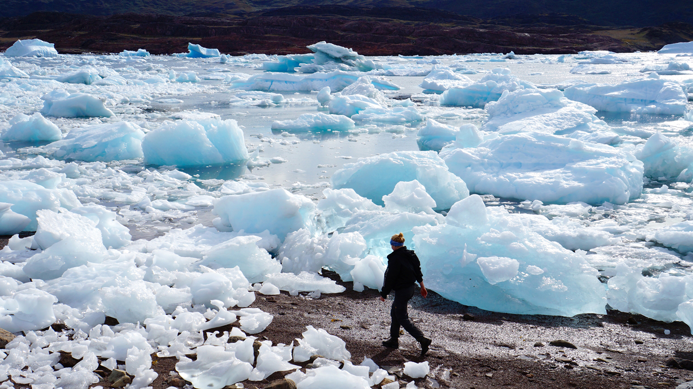 Kvinde går mellem store isflager, som er skyllet på land.
