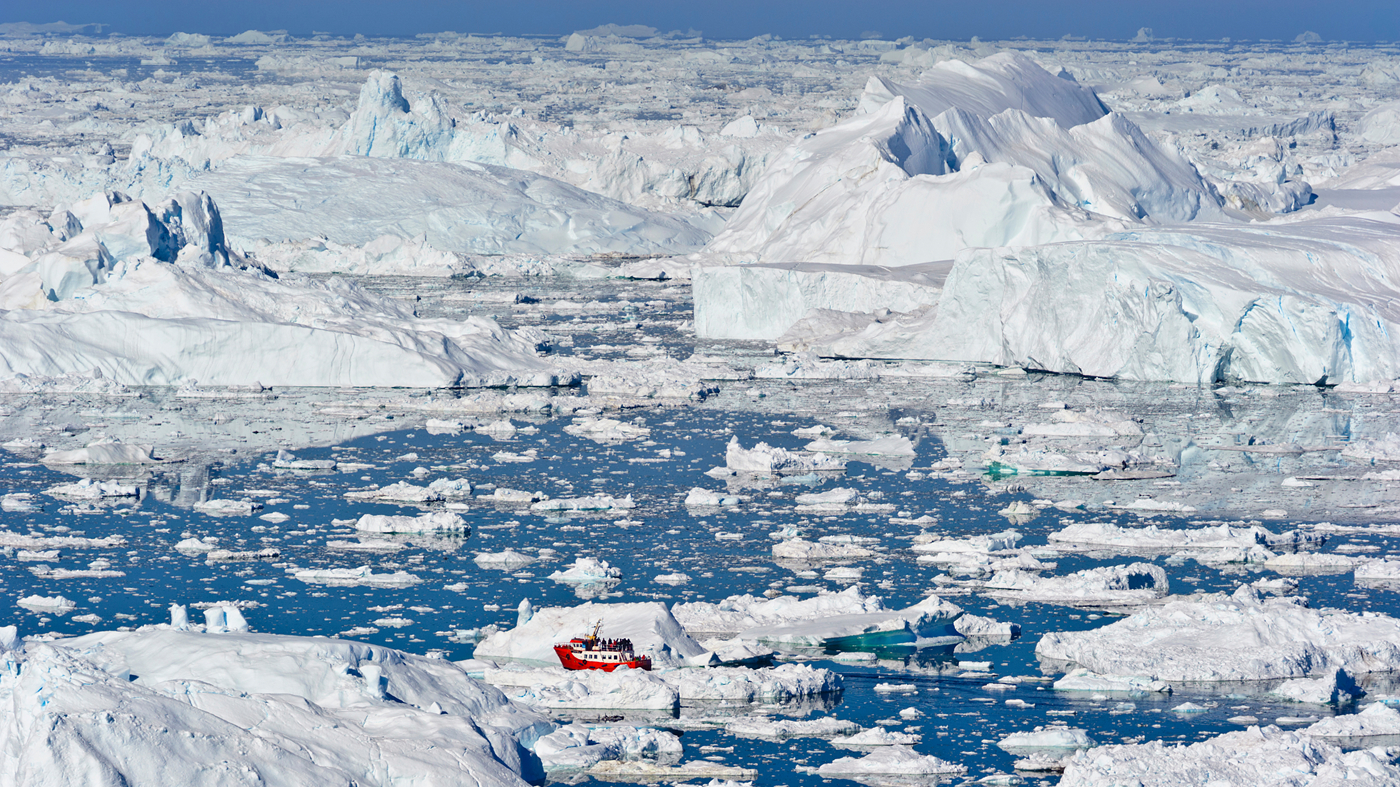 En rød færge ser ubetydeligt lille ud i sammenligning med Grønlands gigantiske isbjerge.