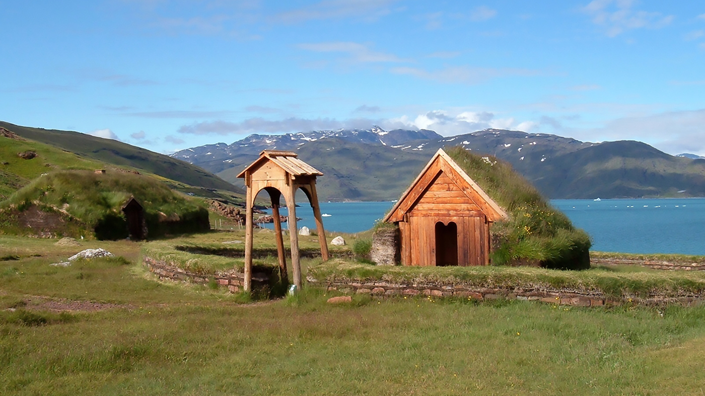 Træstrukturer med fjord og bjerge i baggrunden. Rekonstruktioner af Brattahlid – Erik den Rødes egen gård i Qassiarsuk