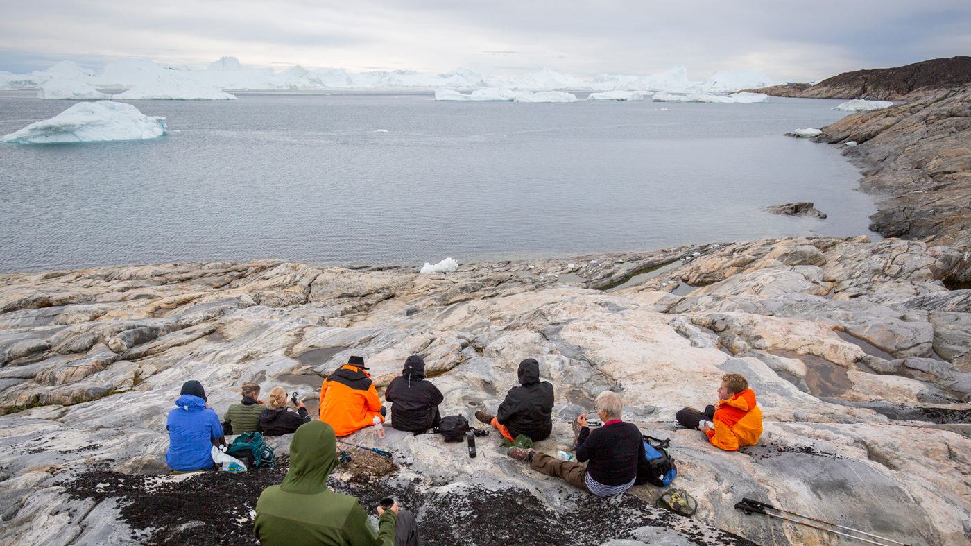 Gæster nyder udsigten over fjorden, mens isbjergene flyder forbi.