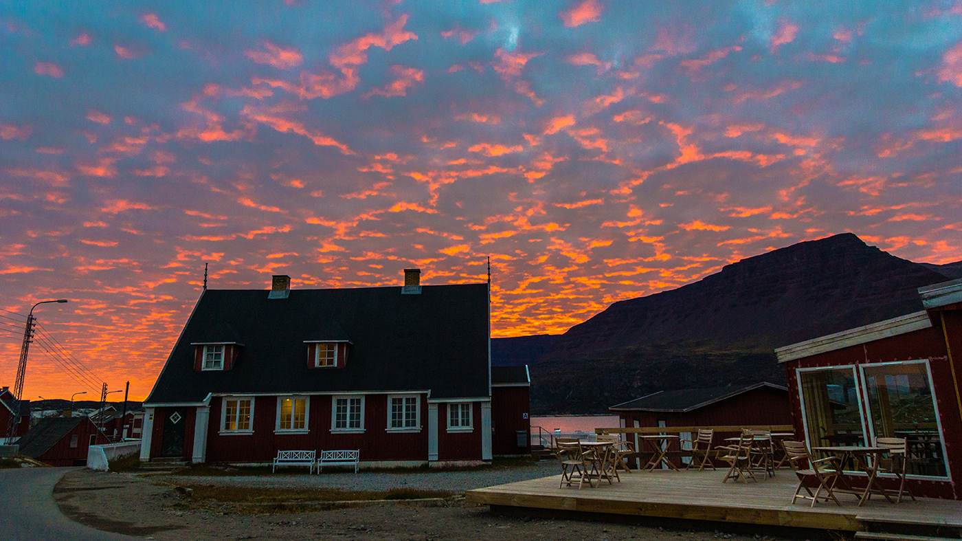 Hotel Disko Islands hovedbygning med bjerge og blodrød himmel i baggrunden.