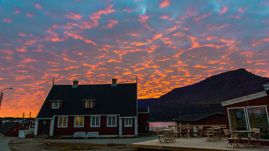 Hotel Disko Islands hovedbygning med bjerge og blodrød himmel i baggrunden.