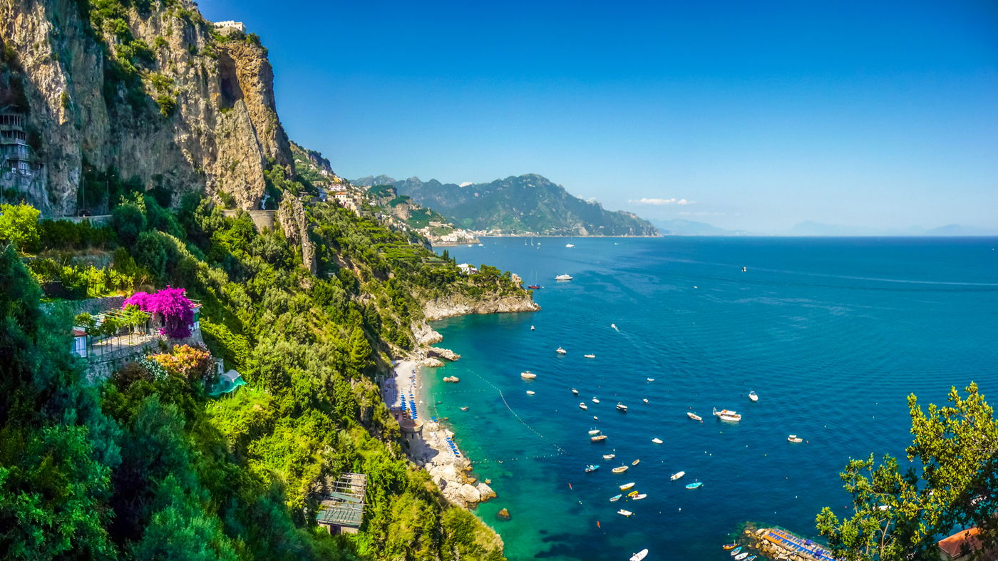Udsigt fra Amalfi, med frodige bjerge, klar himmel, hvide strande, krystalblåt hav og både. 