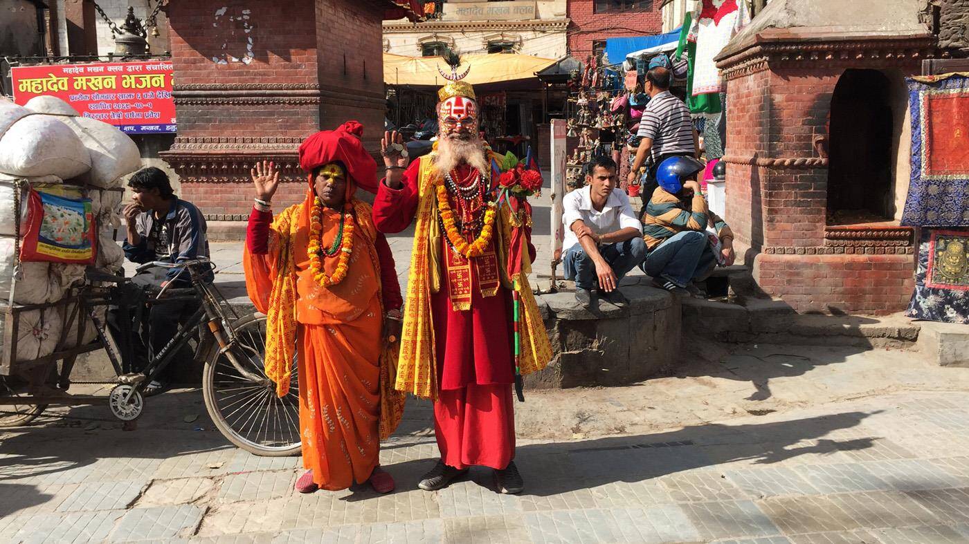 Farverig lokalbefolkning i Kathmandu - en mand og kvinde i røde og orange klæder og ansigtsmaling. 