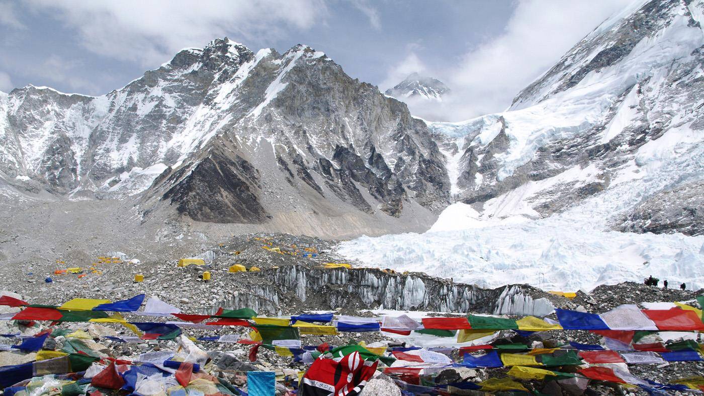 Everest Basecamp med farverige flag og telte, store dynger sne, og skarpe bjergtinder. 