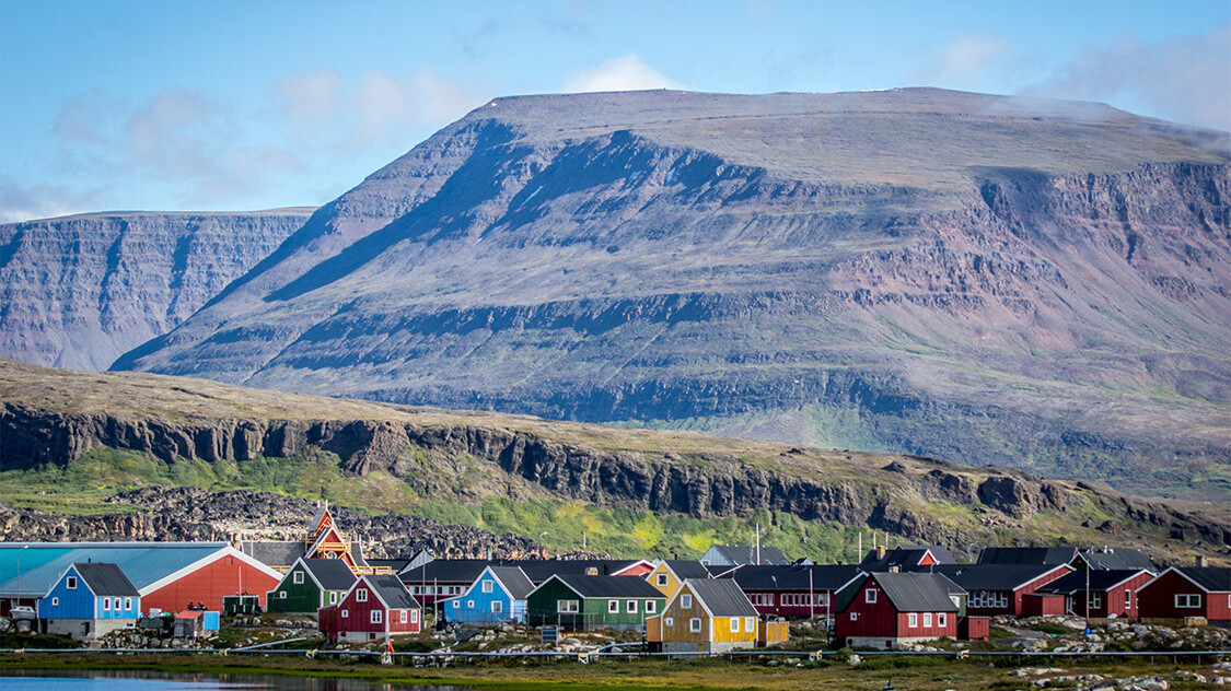 Grønlandsk by med huse i flere forskellige farver og stort granitfjeld i baggrunden