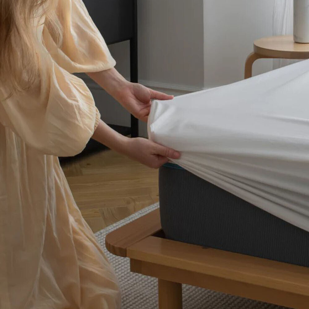 En kvinde er ved at beklæde en seng med et stræklagen i hvid. Stræklagenet er fremstillet i bomuld i en god kvalitet.