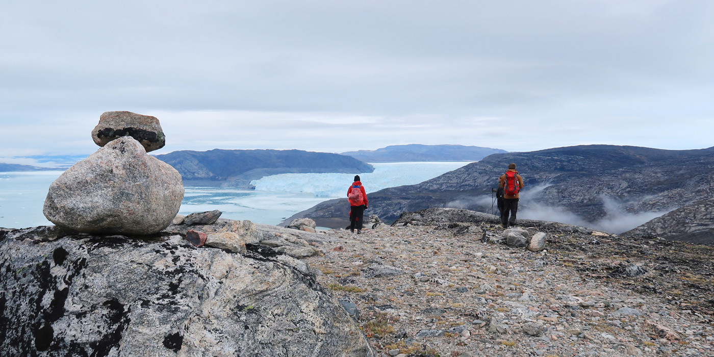 To personer i røde frakker nyder udsigt fra bjergtop over Eqi-gletsjeren. 
