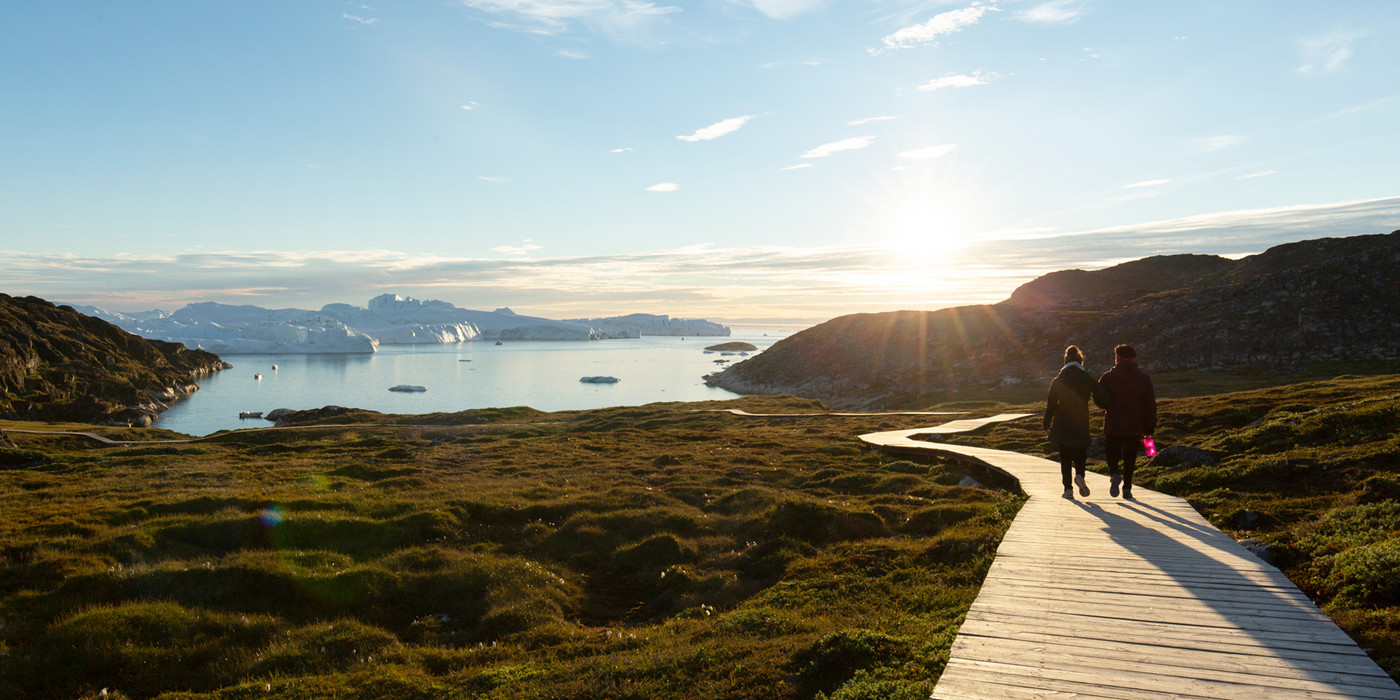 To personer gå langs gangbro ud mod fjorden.