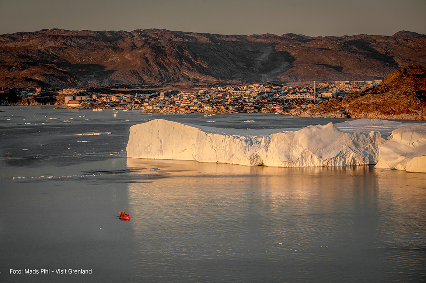 Ilulissat set fra vandsiden med stort isbjerg i forgrunden