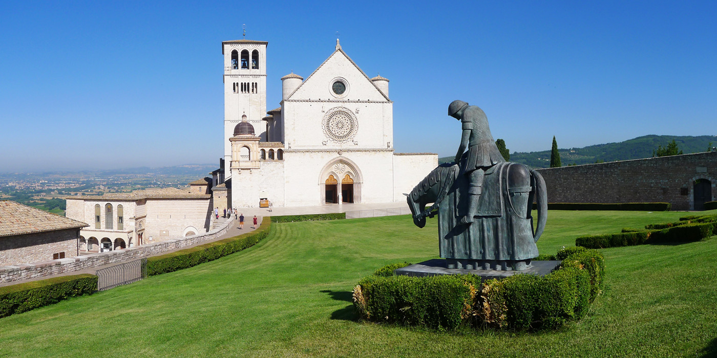 San Francescos hvide kirke i romersk-gotisk stil med statue af ridder på hest i forgrunden og udsigt over byen i baggrunden.