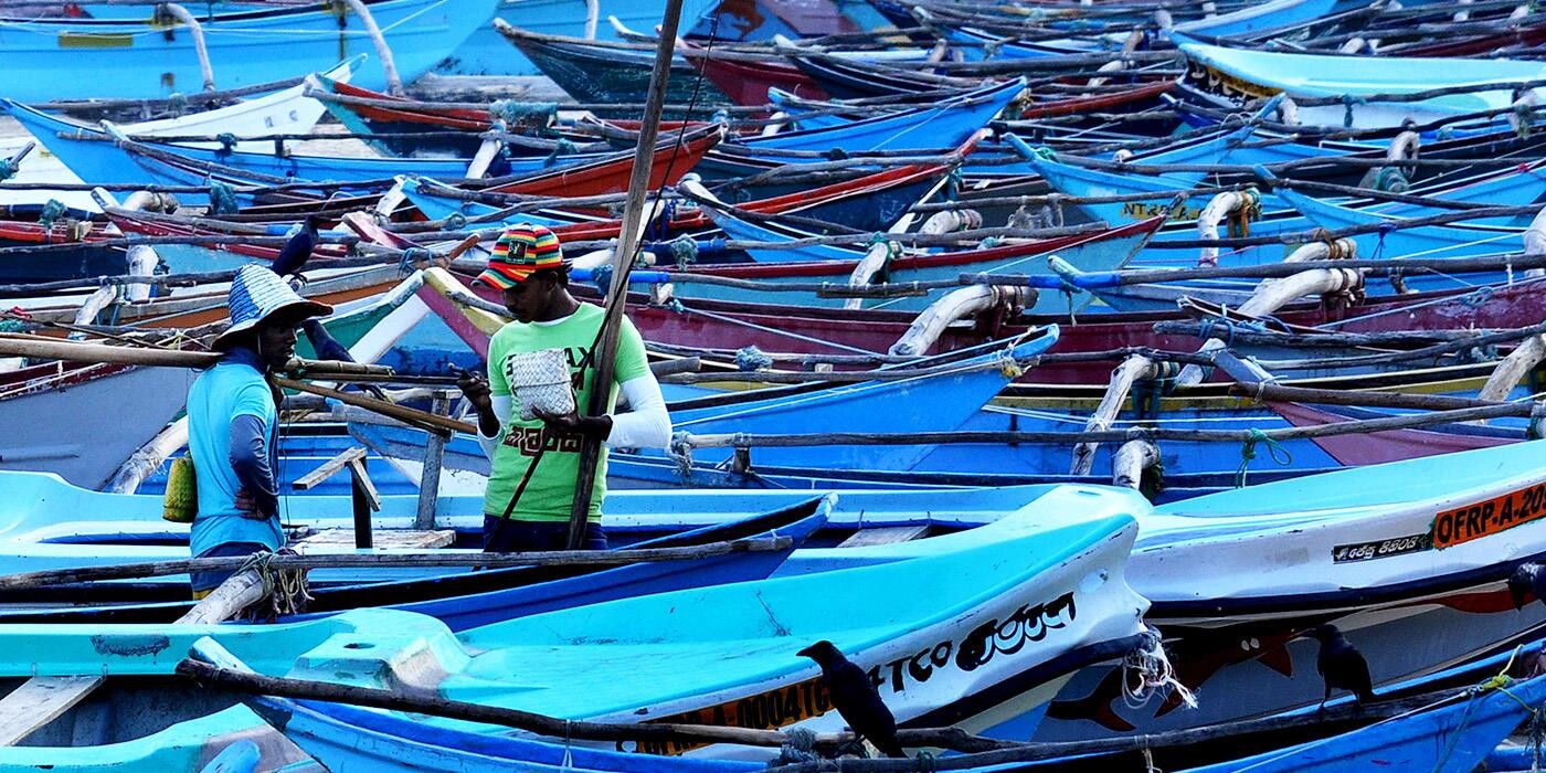 To mænd står omgivet af blå både i Negombo