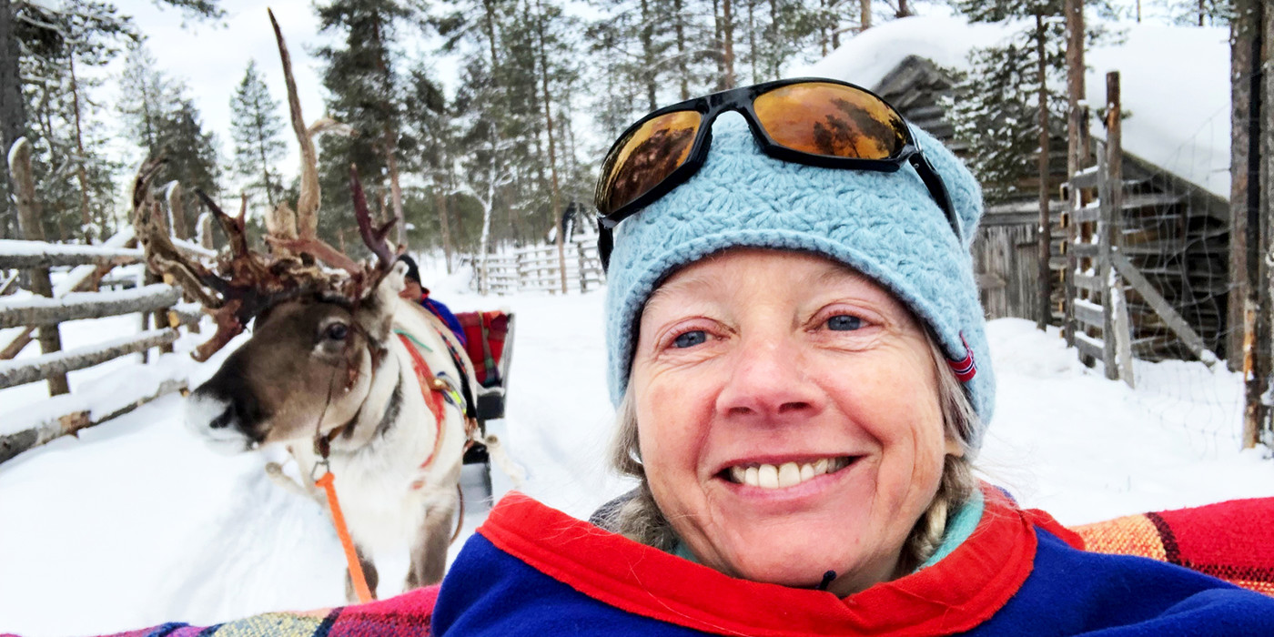 Selfie af en smilende Camilla Hvalsøe klædt i samerfarver, med rensdyr i baggrunden.