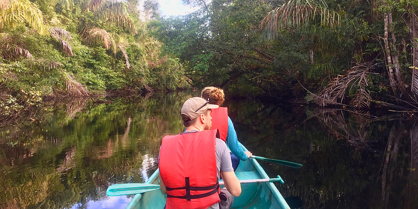 To personer sidder i båd med padler i hænderne på flod, omkredset af regnskov.
