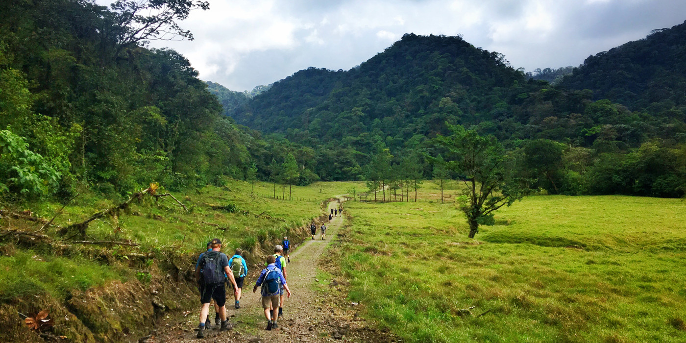 Gruppe vandrer gennem dal omgivet af frodige bjerge. 
