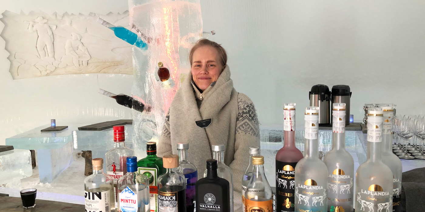 Kvinde i Saariselkas isbar ved Northern Lights Village. I forgrunden ses stor udvalg af finsk/nordisk alkohol, og i baggrunden ses borde, bænke og vægudsmykning, som alt sammen er skåret i is. 