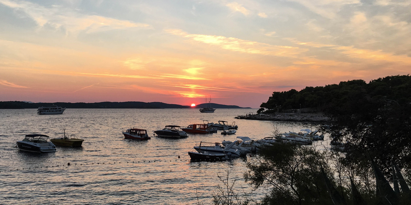 Solopgang over bjergkam i horisonten, med hav og både i forgrunden.