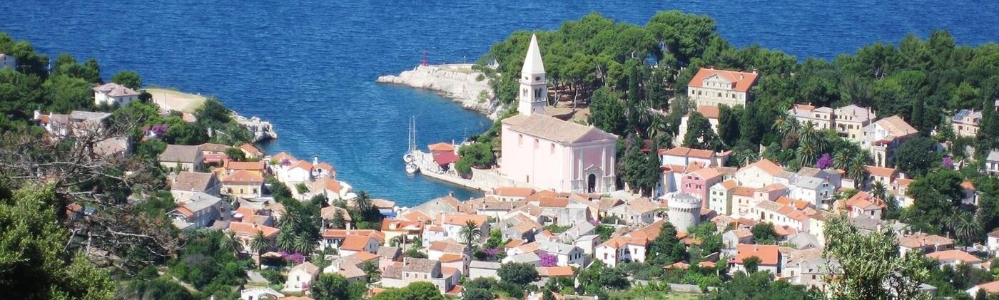 Kystby i Kroatien med træer, kirke og skibe i havnen.