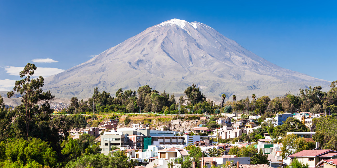 Byen Arequipa med hvide huse, træer og gigantisk vulkan med sneklædt top i baggrunden.