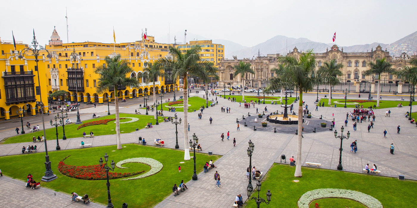 Plads i Lima med mange mennesker, høje palmer og flotte bygninger. 