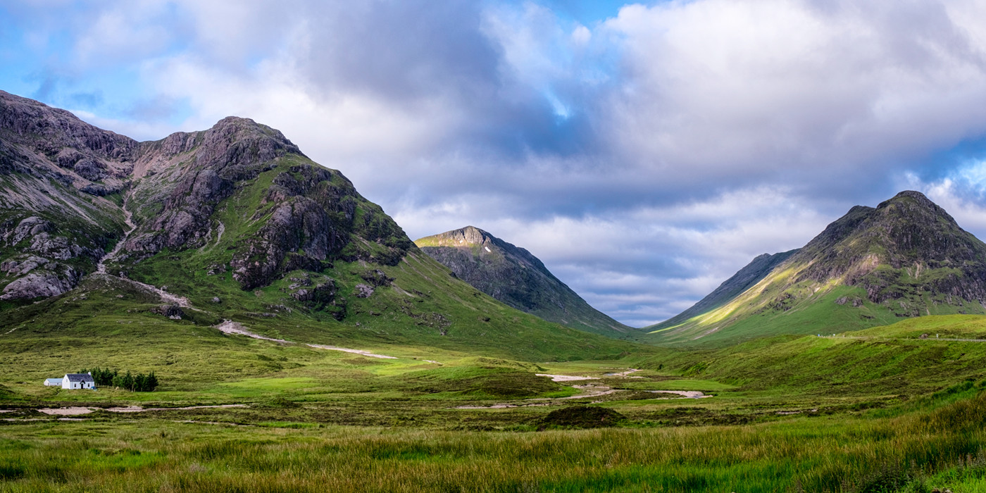 Bjergmassivet Buachaille Etive Beag med et lille, hvidt hus foran. 