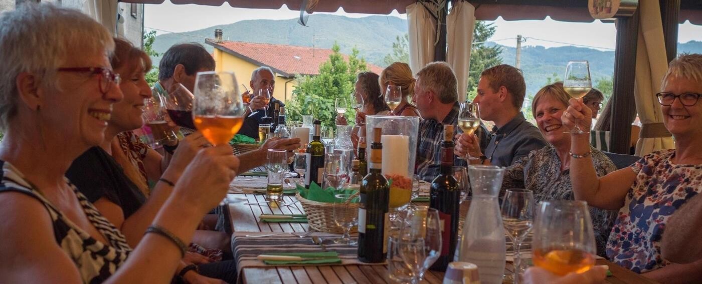 Smilende gæster skåler med hvidvin ved det italienske middagsbord. 