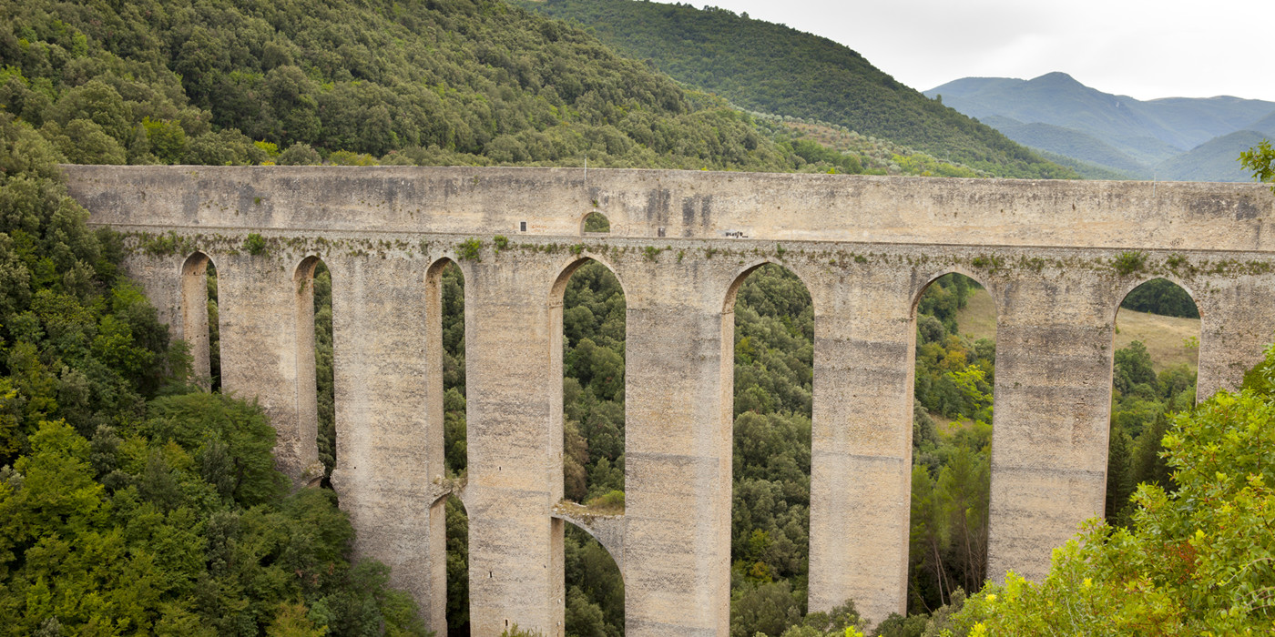Ponte delle Torri, en gammel romersk akvædukt-bro, står højt over en dal og fører til en bjerg dækket af frodig skov.