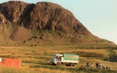 Lastbil holder parkeret i dal med bjerge i baggrunden og et lille telt i forgrunden. 