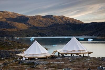 Glamping-telte ved Camp Kangiusaq med udsigt over sø med små isbjerge.