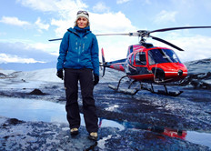 Foto af Mette Lund Haywood i Grønland, med helikopter i baggrunden.