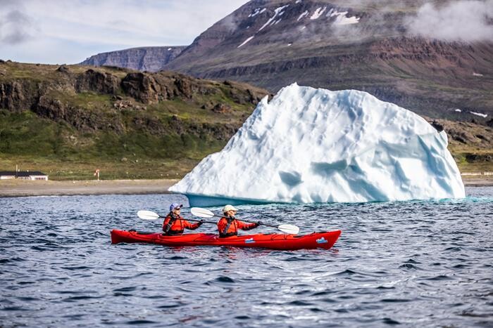 2-person kayak with instructor. In the the near background there is an iceberg, and in the far background there is a big mountain. 
