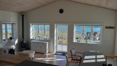 Villa living room with sofa, stove, dining table and view of the fiord and mountains of Igaliku.